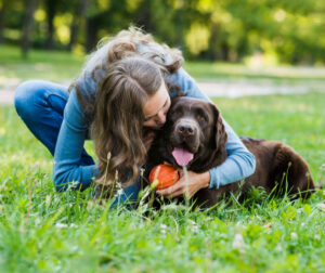 mujer joven abraza a perro con pelota sobre la hierba